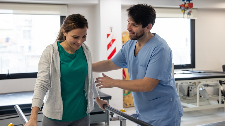A friendly Allied Health services worker guides a person using equipment while they undergo physical therapy