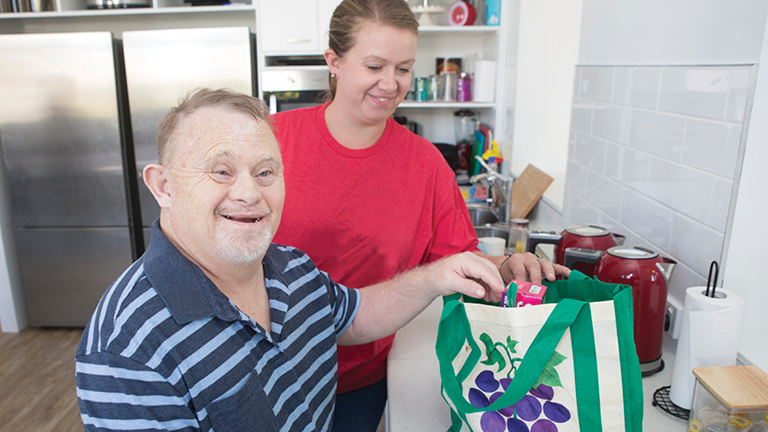 A support worker helps a person unpack groceries in their kitchen