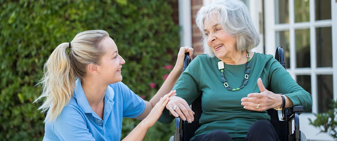 A smiling health services worker supports an elderly person while walking